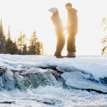 Ein Paar steht im Sonnenlicht an den verschneiten Pine Point Rapids im Whiteshell Provincial Park