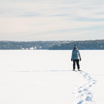 Eine Frau ist im Riding Mountain National Park auf Schneeschuhen auf einem zugefrorenen See unterwegs. 