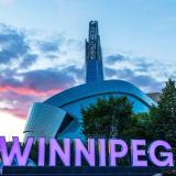 Das architektonisch eindrucksvolle Gebäude des Canadian Museum for Human Rights. Im Vordergrund in großen Leuchtbuchstaben der Schriftzug "Winnipeg"