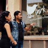 Ein Paar steht in den Straßen des Exchange Districts und betrachtet eine bunte Graffiti Wand, auf der eine Hinweistafel zur Geschichte des Viertels installiert wurde.