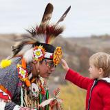 Ein kleiner Junge darf im Wanuskewin Heritage Park den Kopfschmuck eines indigenen Tänzers berühren.